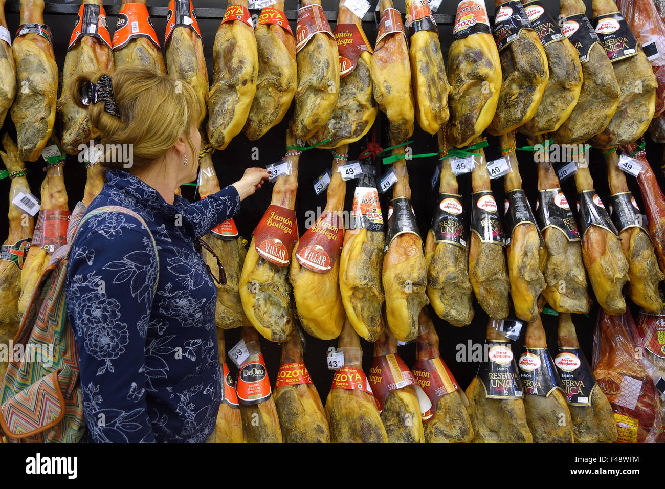 Woman shopper shopping buying Cured hams Jamon Iberico iberian Ham Hanging in Spain Spanish supermarket Stock Photo