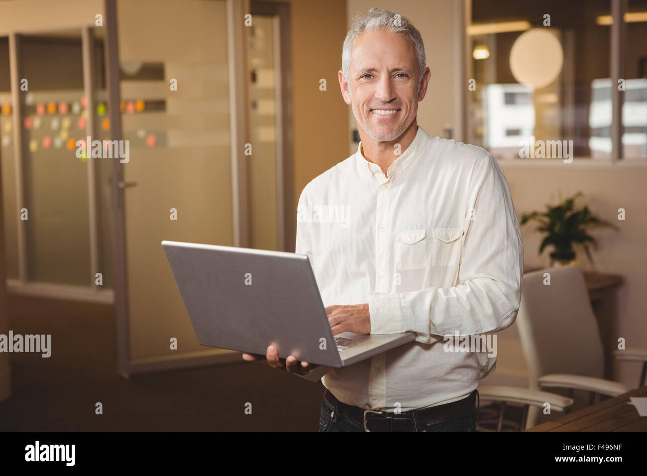 Portrait of happy businessman using laptop in creative office Stock Photo