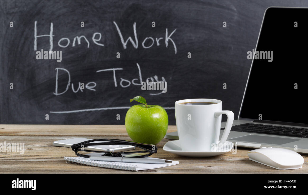 Front view of teachers desktop with laptop, paper, pen, coffee, reading glasses, mouse, cell phone and green apple. Stock Photo