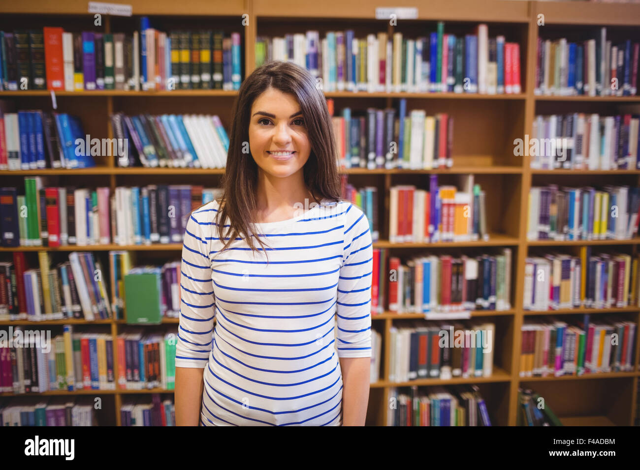 Happy female student against bookshelf Stock Photo