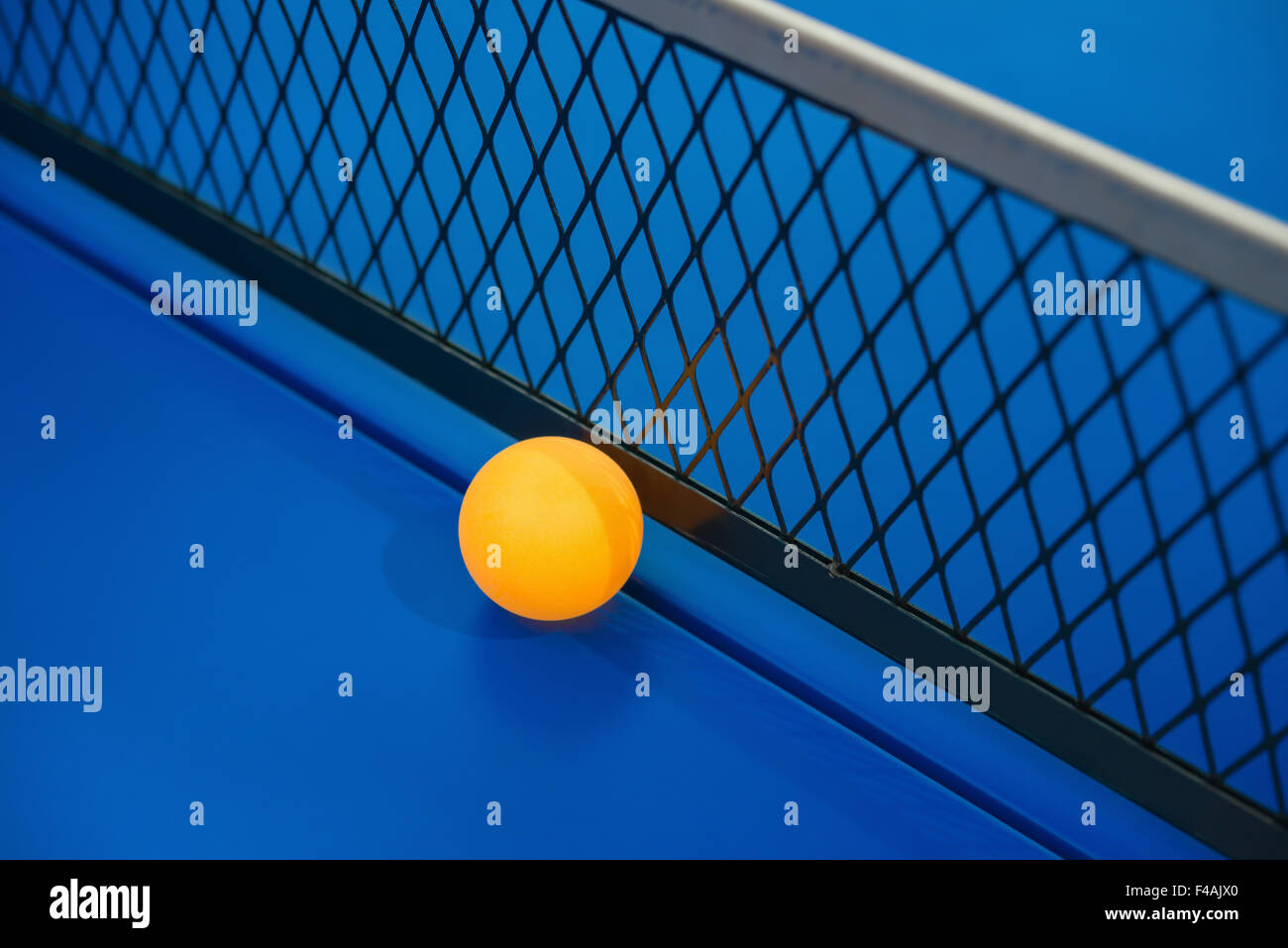 yellow ball hits the bottom of the net on a blue pingpong table Stock Photo