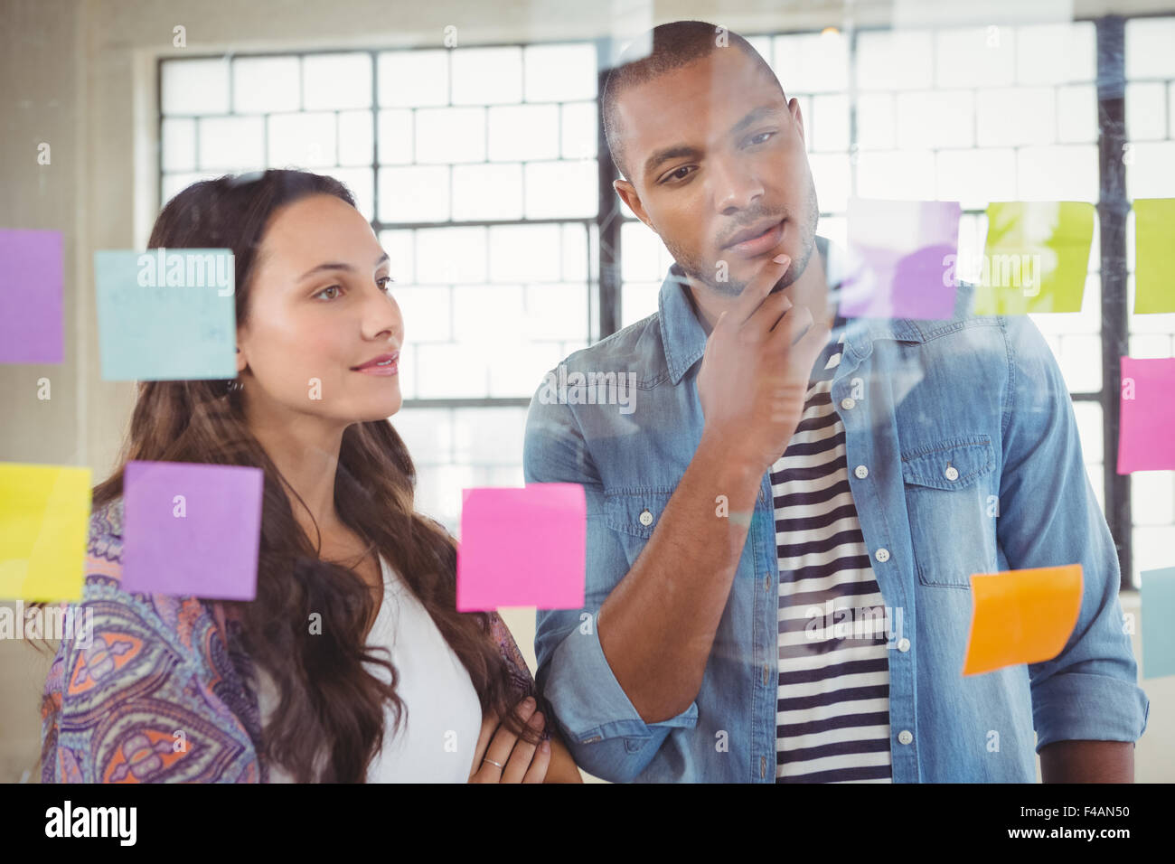 Colleagues looking at sticky notes on glass window Stock Photo