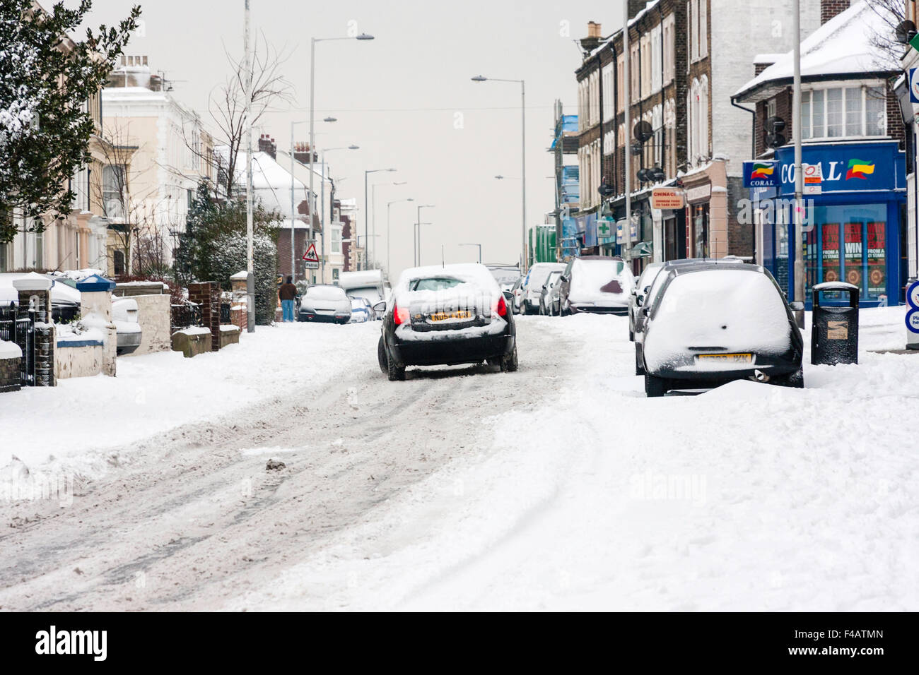 Bad weather, England, Ramsgate town. Snow covered main road with cars parked and car attempting to drive along in hazadous conditions after snowfall. Stock Photo