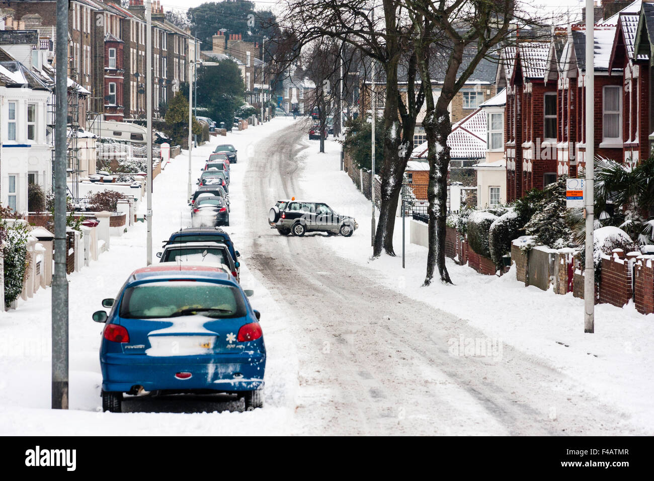 Bad weather, England, Ramsgate town. Snow covered main road with cars parked and car attempting to drive along in hazadous conditions after snowfall. Stock Photo