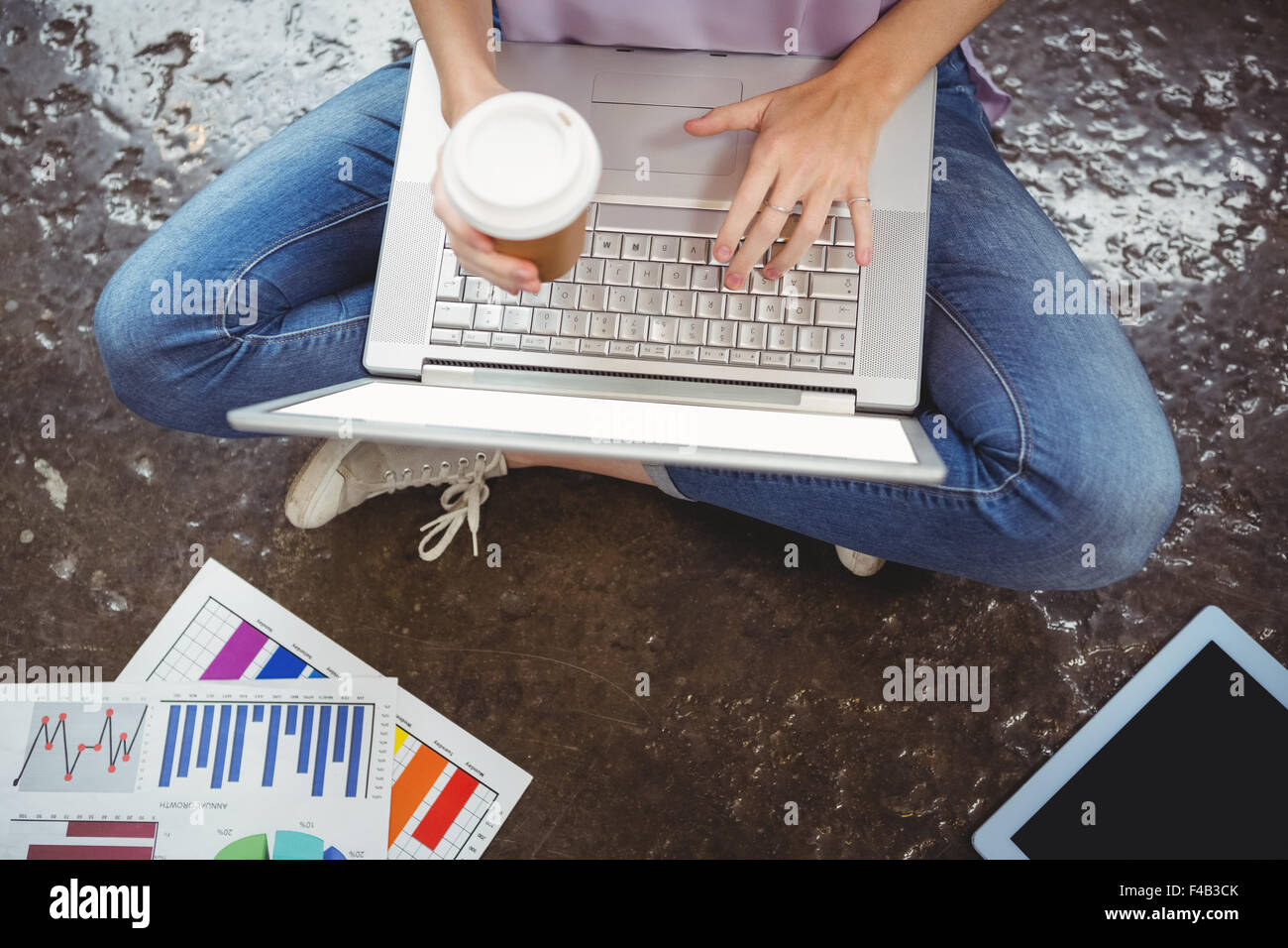 Low section of businesswoman using laptop while holding cup Stock Photo