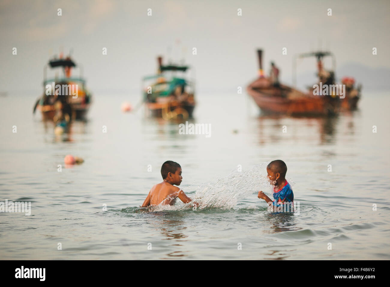 Two boys playing in the sea with long tail boats Koh Phi Phi Don Lei Thailand Stock Photo