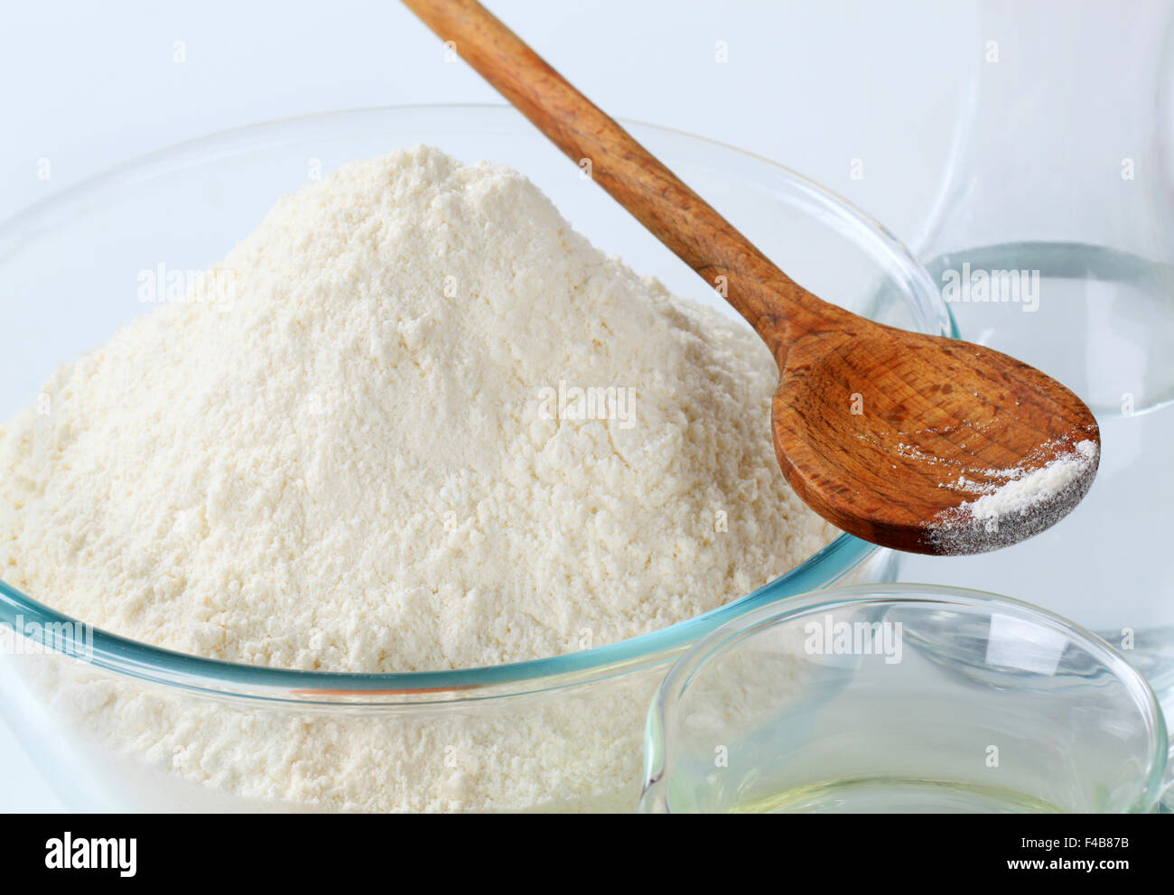 white wheat flour in a glass bowl and a wooden spoon Stock Photo