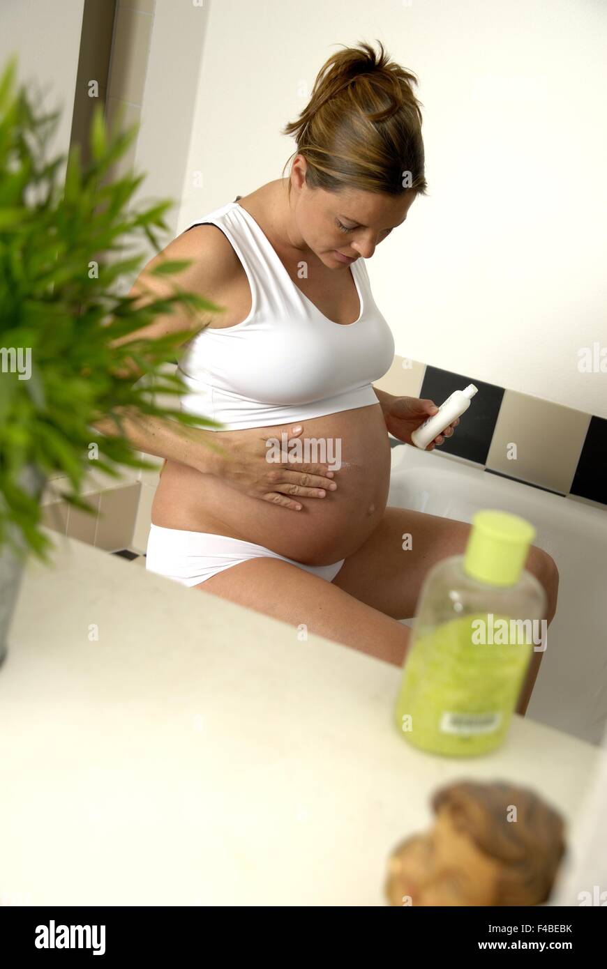 pregnant young woman applying body lotion Stock Photo
