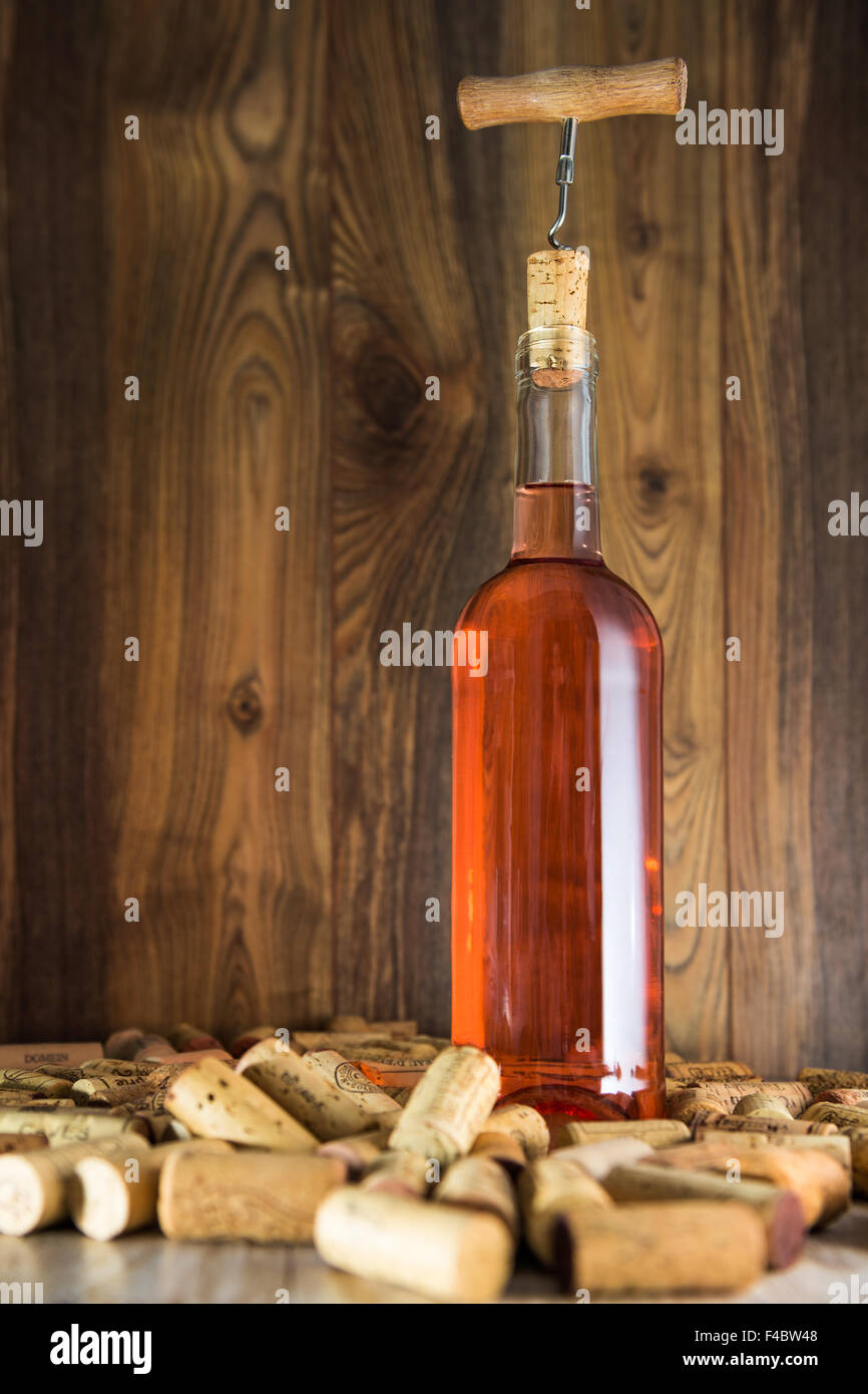 Rose wine in a transparent bottle, cork and a corkscrew on the background boards Stock Photo