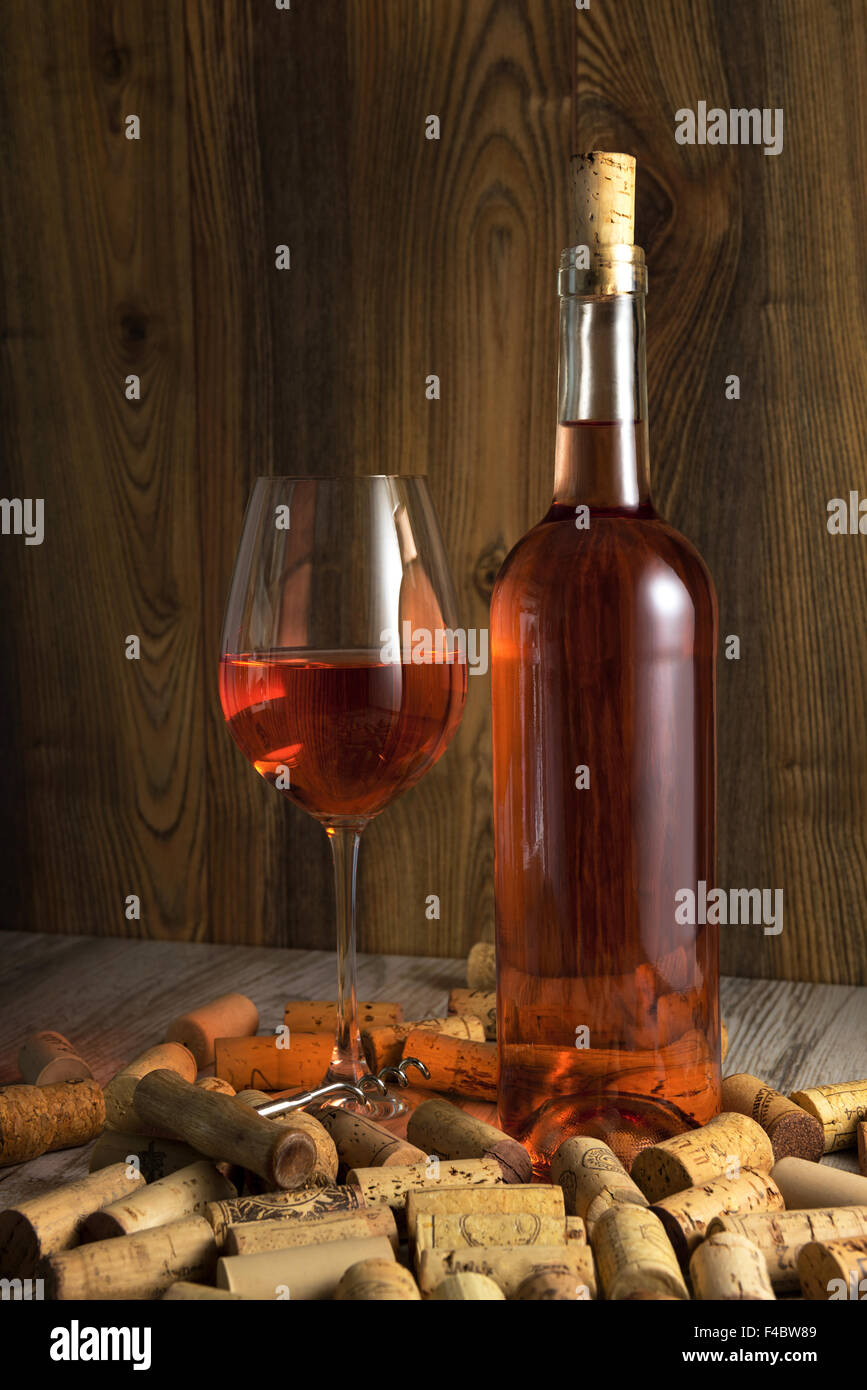 Rose wine in a transparent bottle, glass, cork and a corkscrew on the background boards Stock Photo