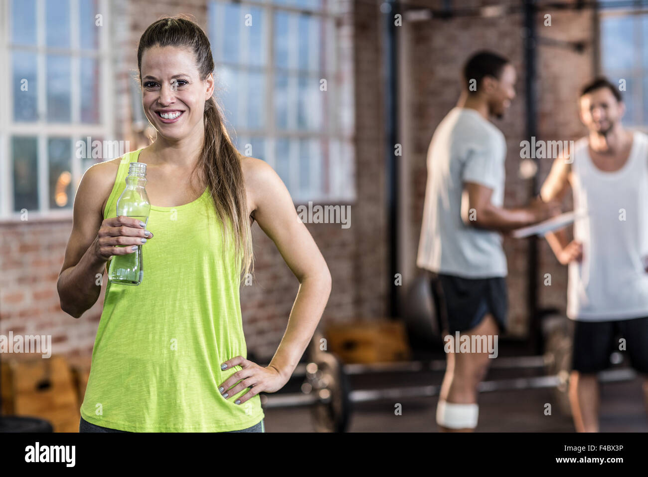 Young woman drinking water from a bottle with colleagues behind her Stock Photo