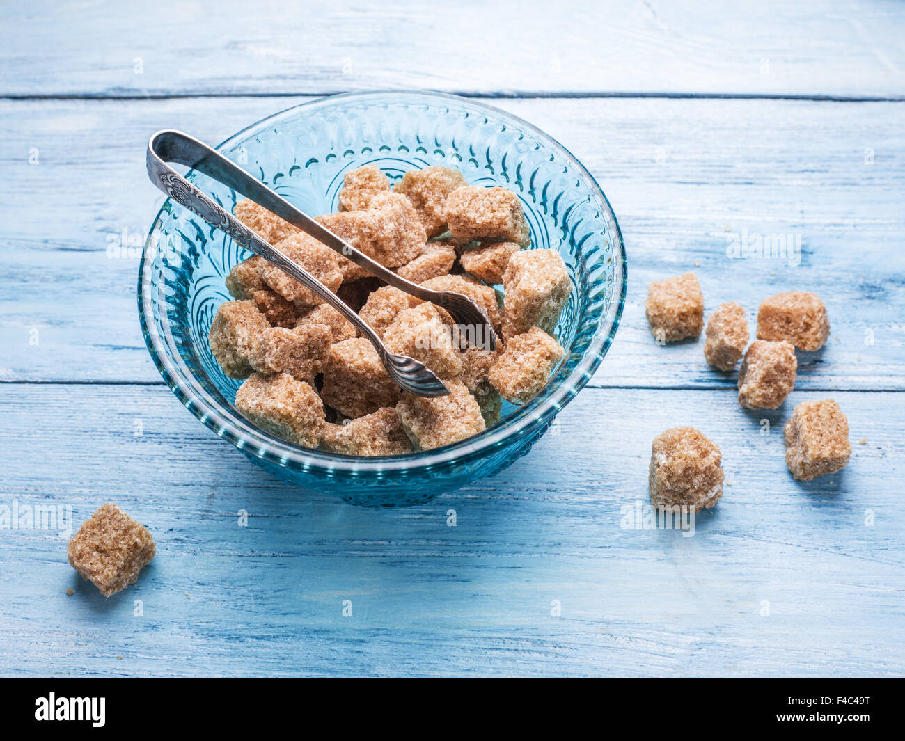 Cane sugar cubes in the old-fashioned glass plate on blue wooden table. Stock Photo