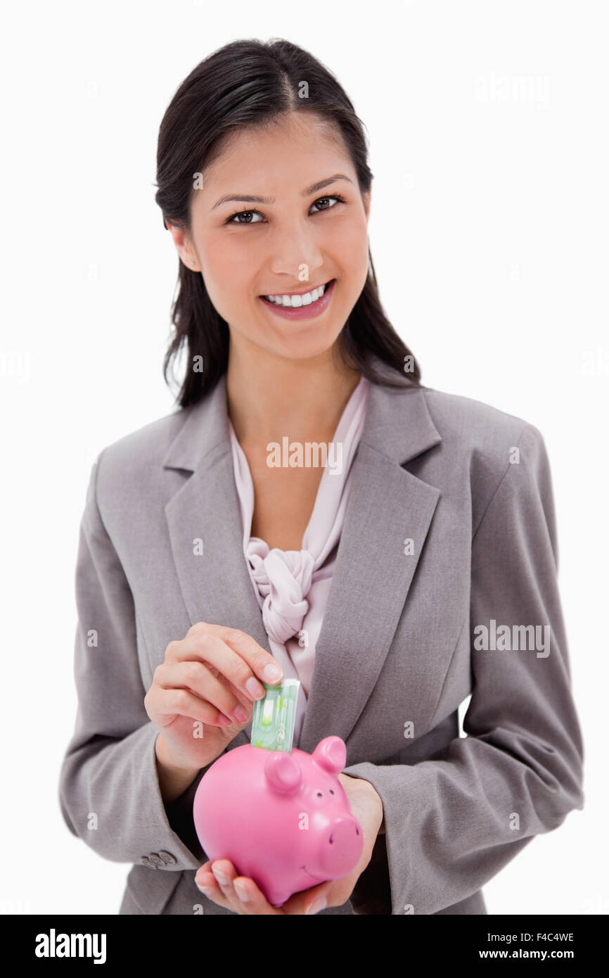 Smiling businesswoman putting money into piggy bank Stock Photo - Alamy