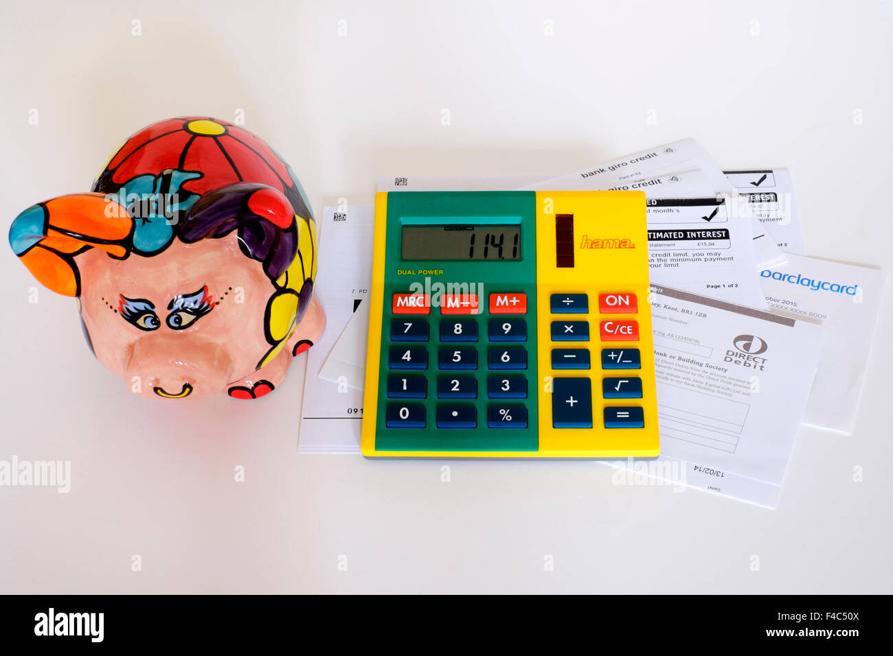 pile of unpaid bills and calculator with piggy bank looking on against a white background england uk Stock Photo