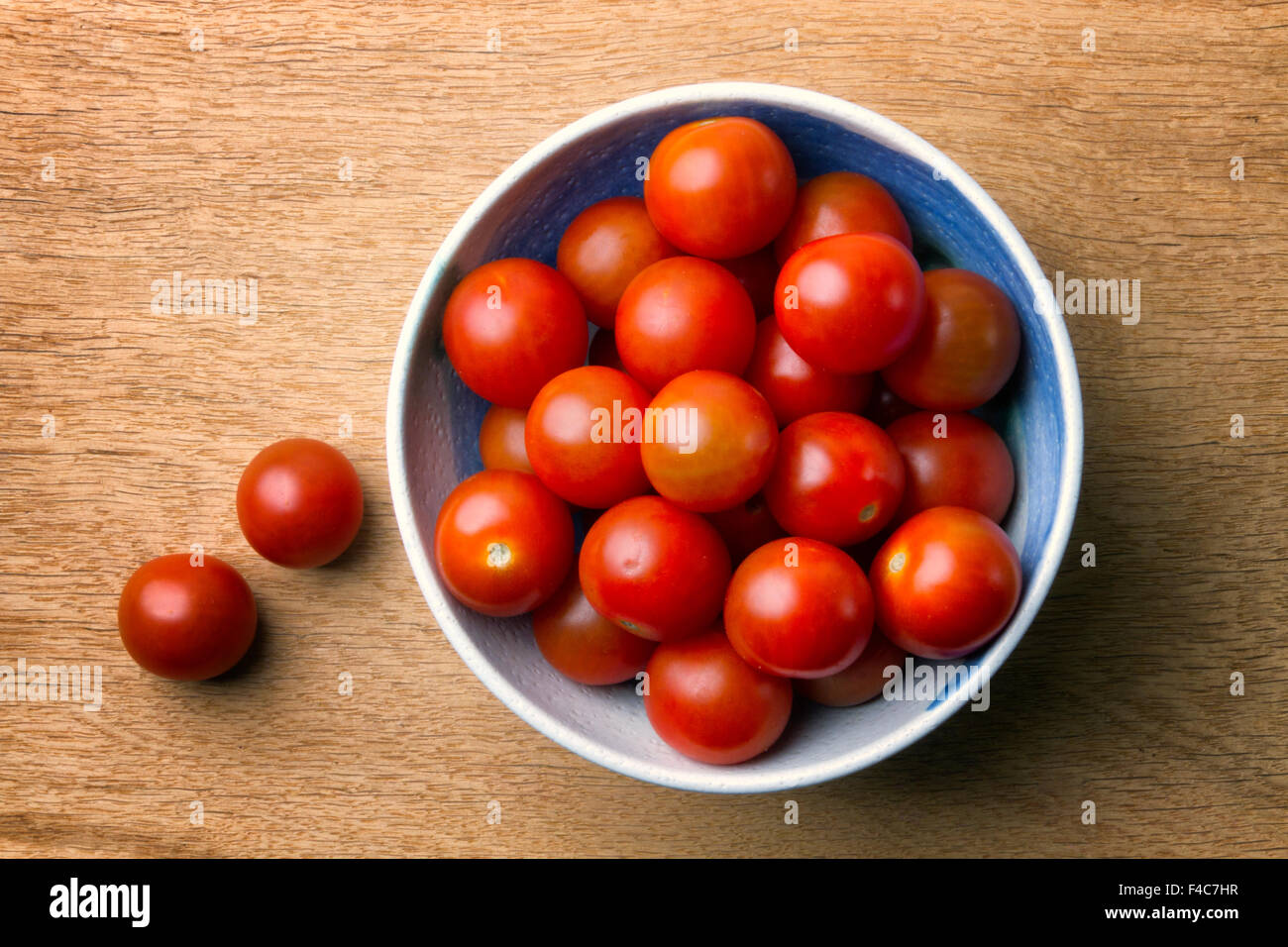 White china bowl with plum tomatoes on a wooden board Stock Photo