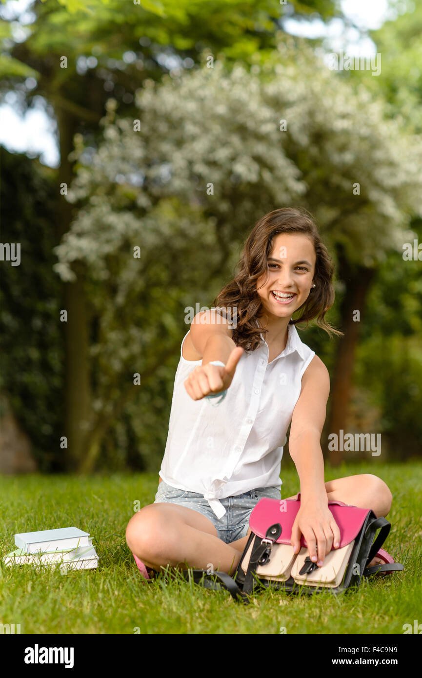 Cheerful student girl sitting grass thumb up Stock Photo - Alamy