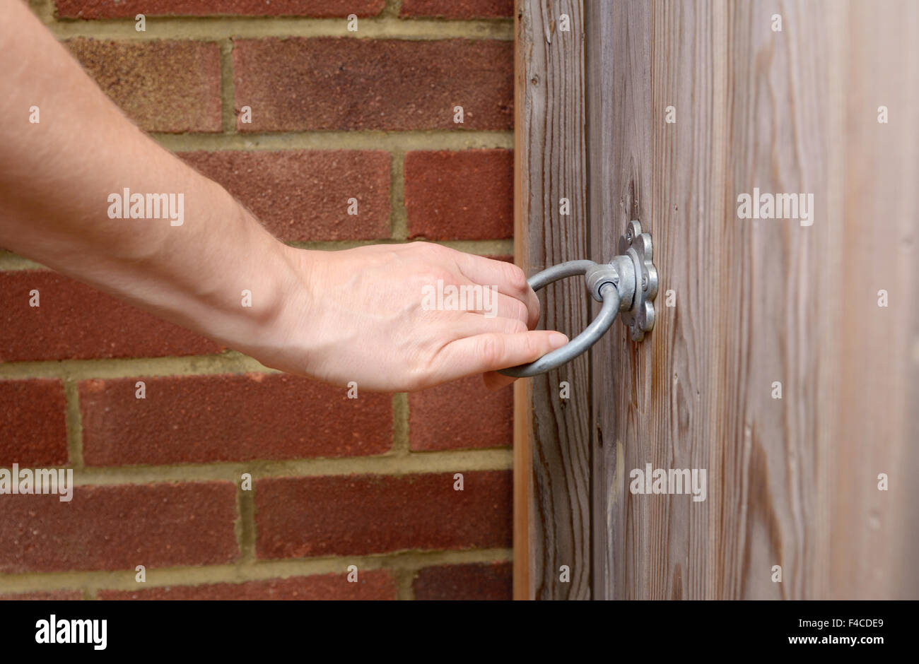 Woman turns a metal ring handle to open a wooden garden gate Stock Photo