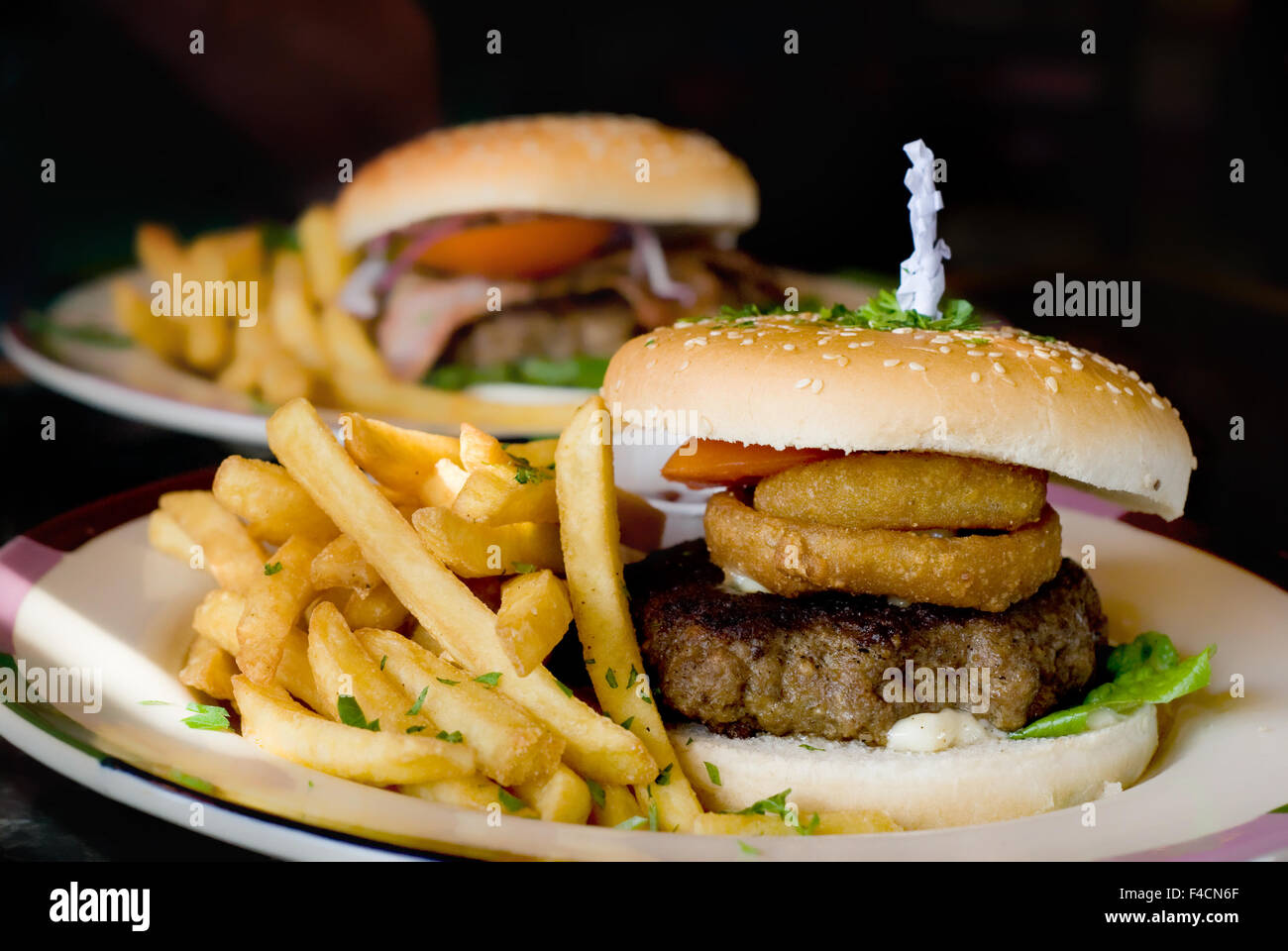Delicious burger bun  with onion rings,salad, and beefburger,served with fries on a plate. Stock Photo