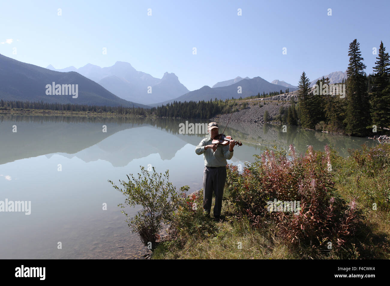Man playing a viola at a  lake with mountainous  background Stock Photo