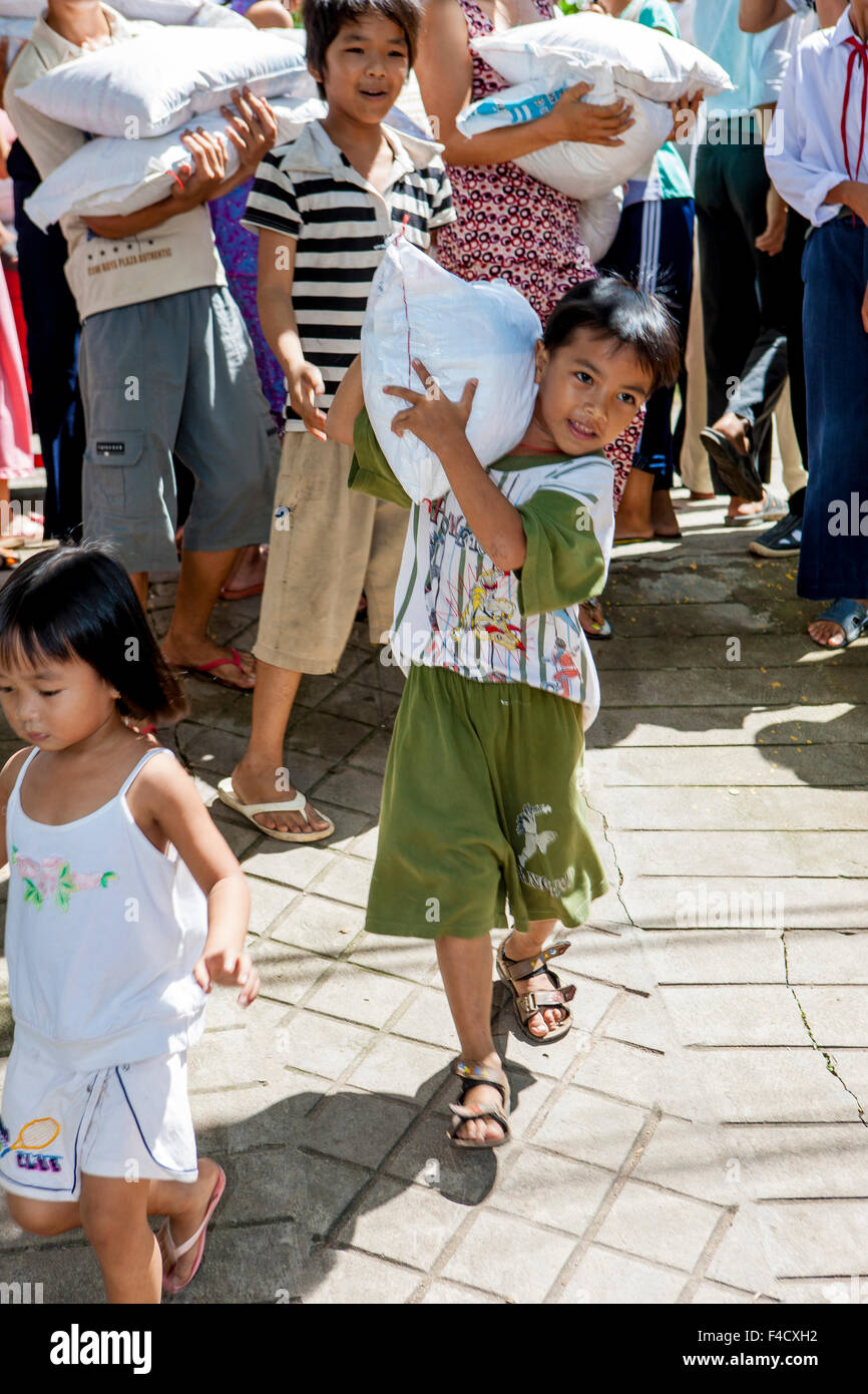 Small boy carrying heavy sack of rice from Donation area. Vietnam
