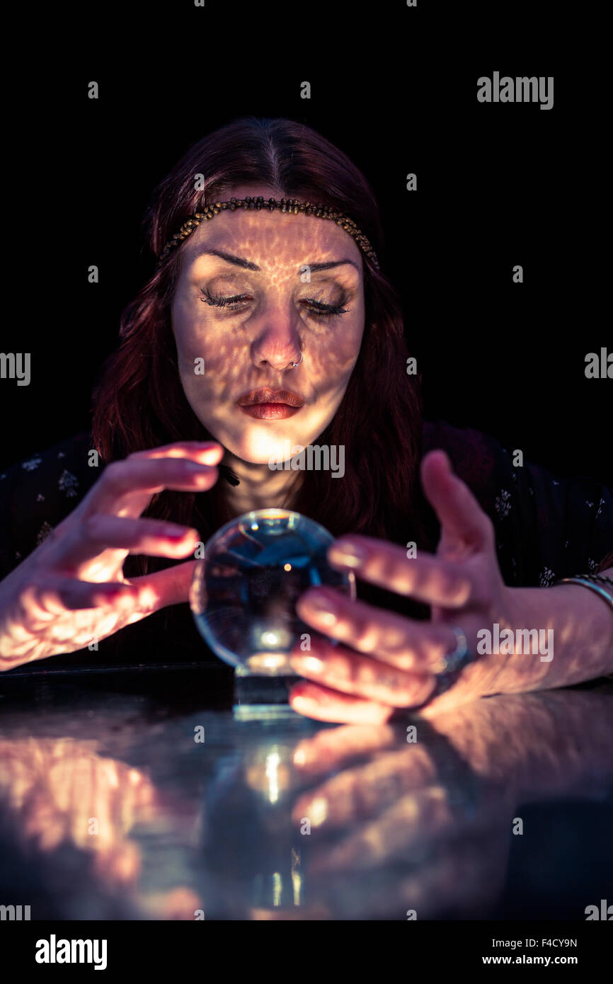 Female fortune teller woman gesturing and using crystal ball with eyes closed Stock Photo