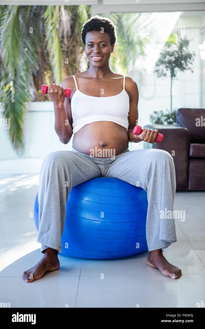 Portrait of smiling pregnant woman with dumbbells sitting on exercise ball Stock Photo