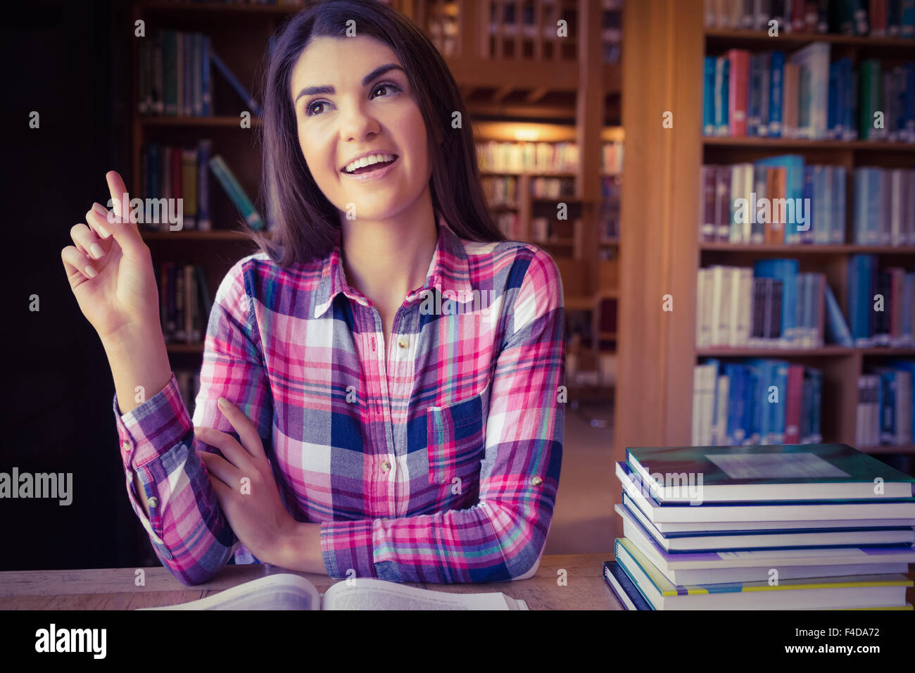 Happy female student at table against bookshelves Stock Photo