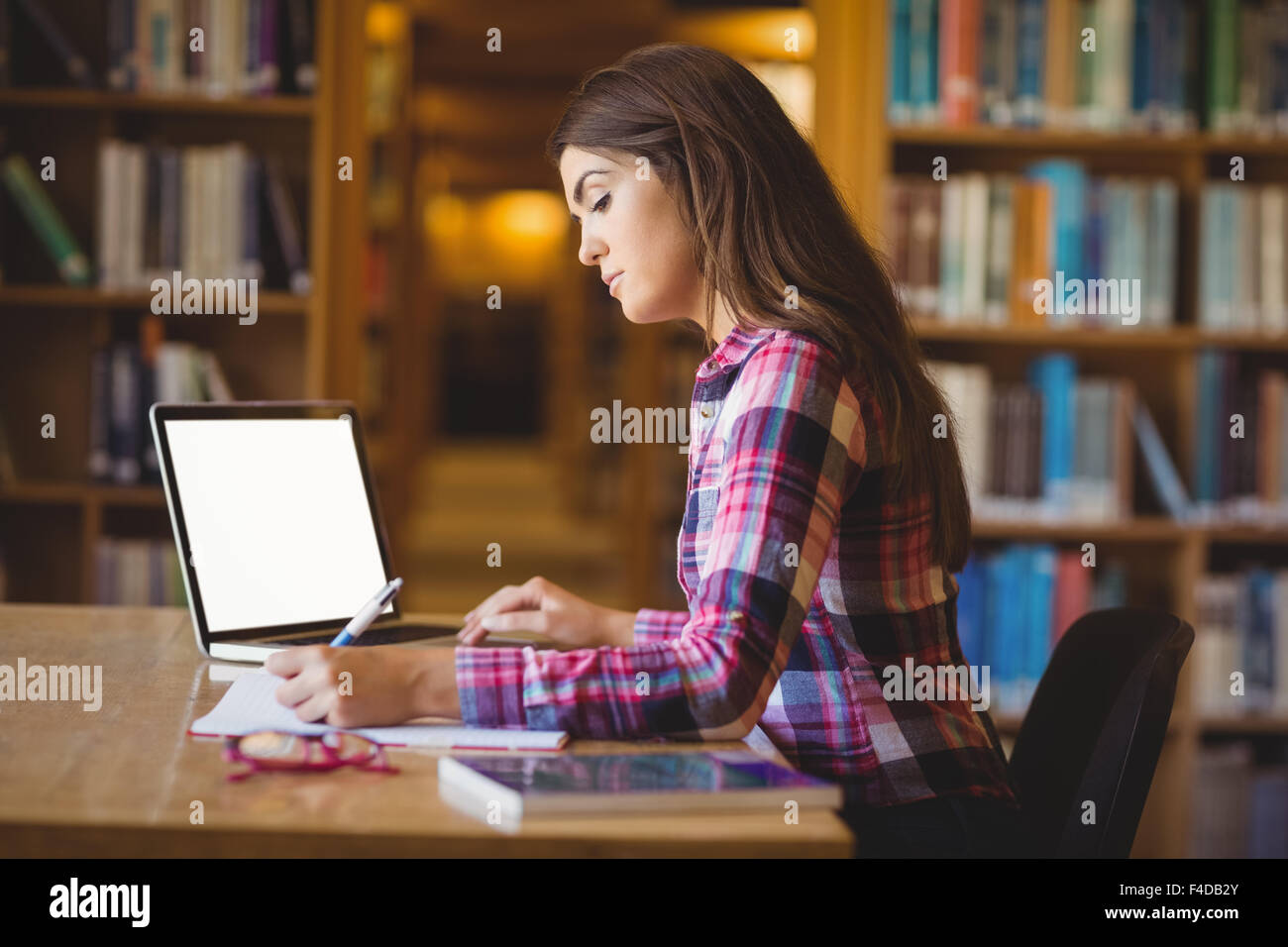 Female student with laptop writing on book Stock Photo