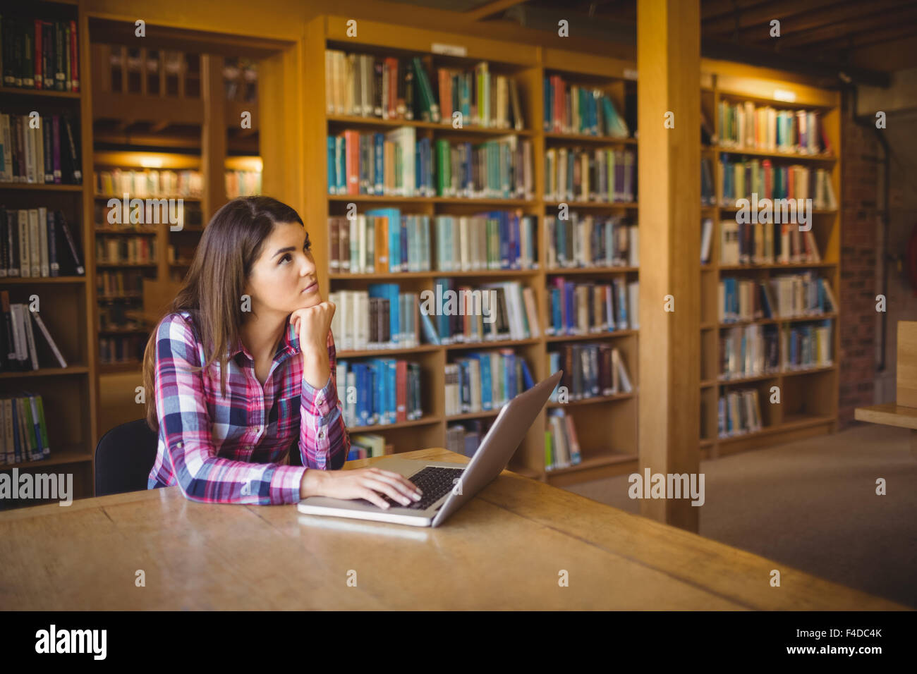 Thoughtful female student with laptopin library Stock Photo