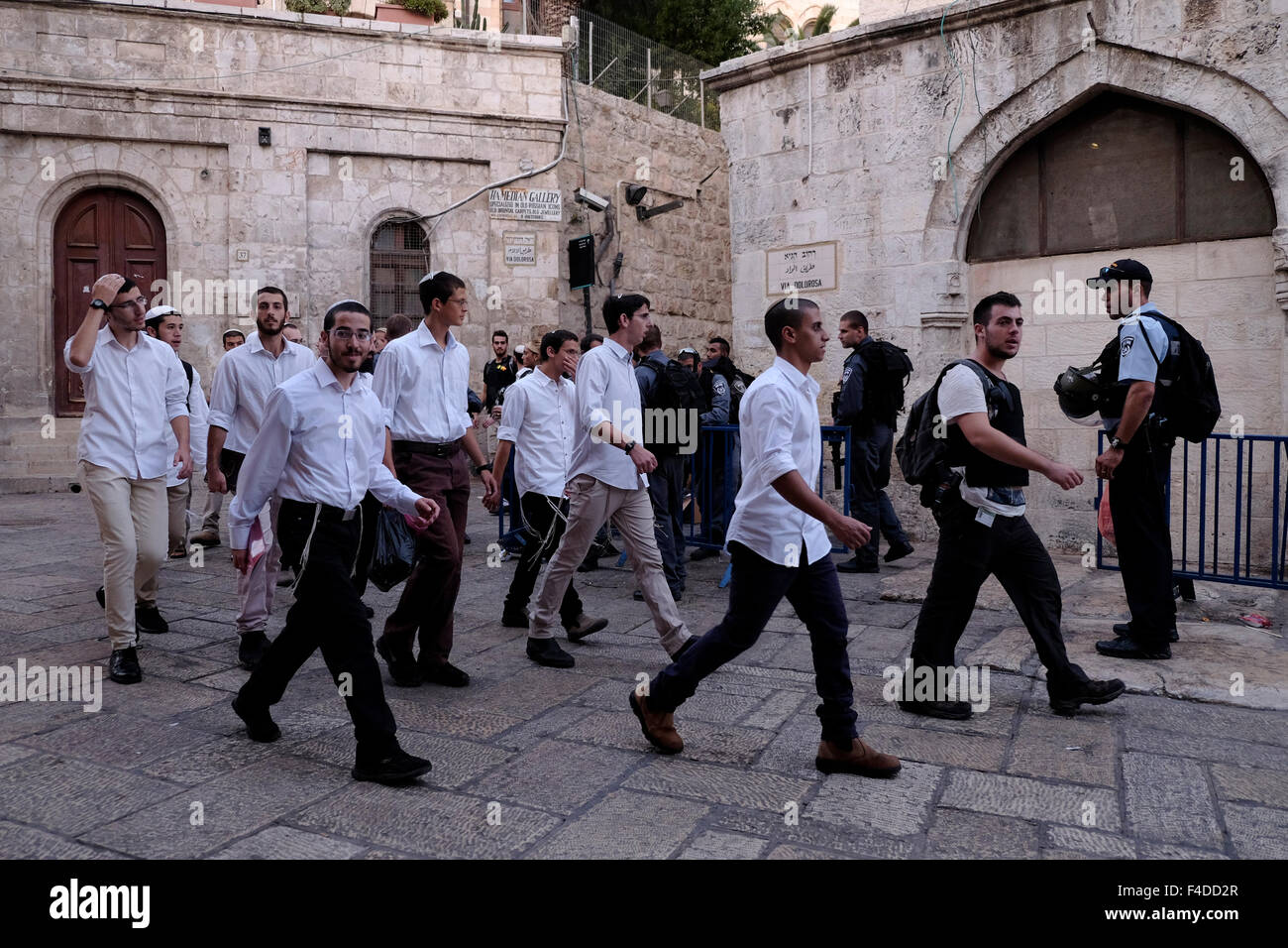 A group of Yeshiva religious Jews walk past Members of the Israeli Security Forces standing guard in Al Wad street which Israelis call Haggai in the Muslim Quarter, old city of Jerusalem Israel Stock Photo