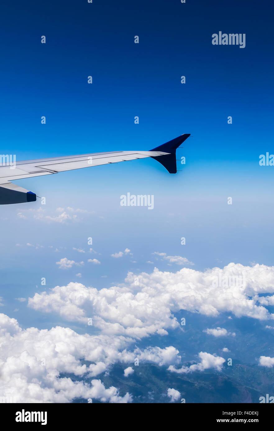 Wing of a Flying Airplane above clouds over Himalayan Mountains Stock Photo