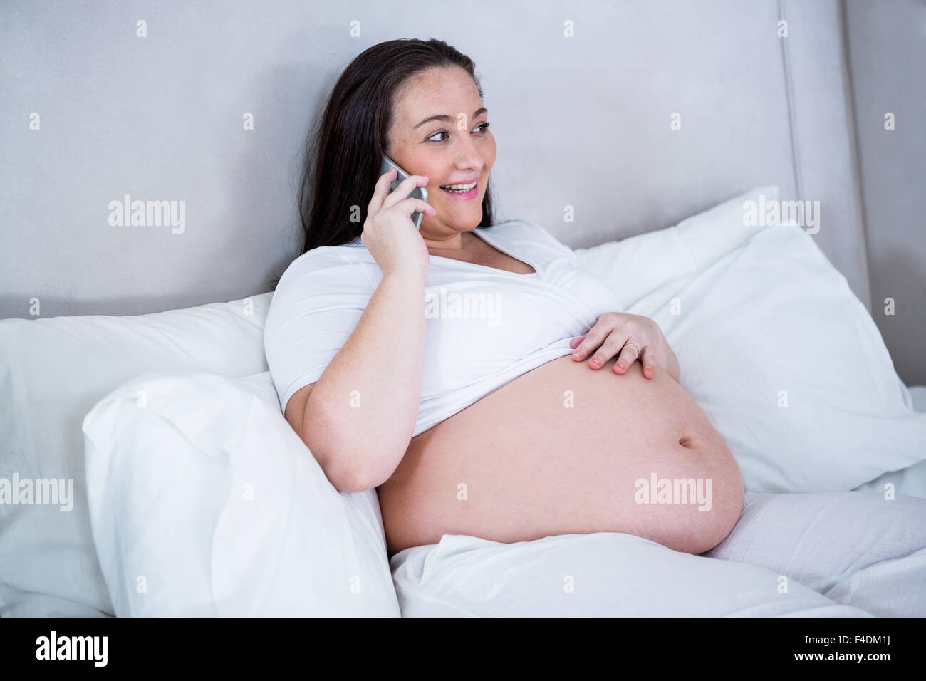 Pregnant woman phoning while lying on bed Stock Photo