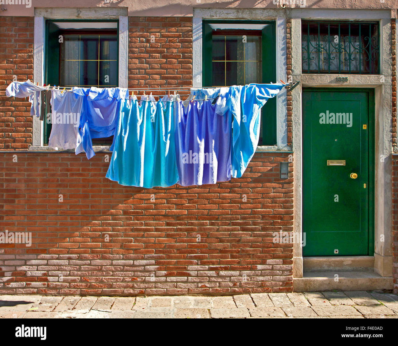 Venice, Italy - Laundry hanging on the clothesline in front of the windows near a green door entrance of a house Stock Photo