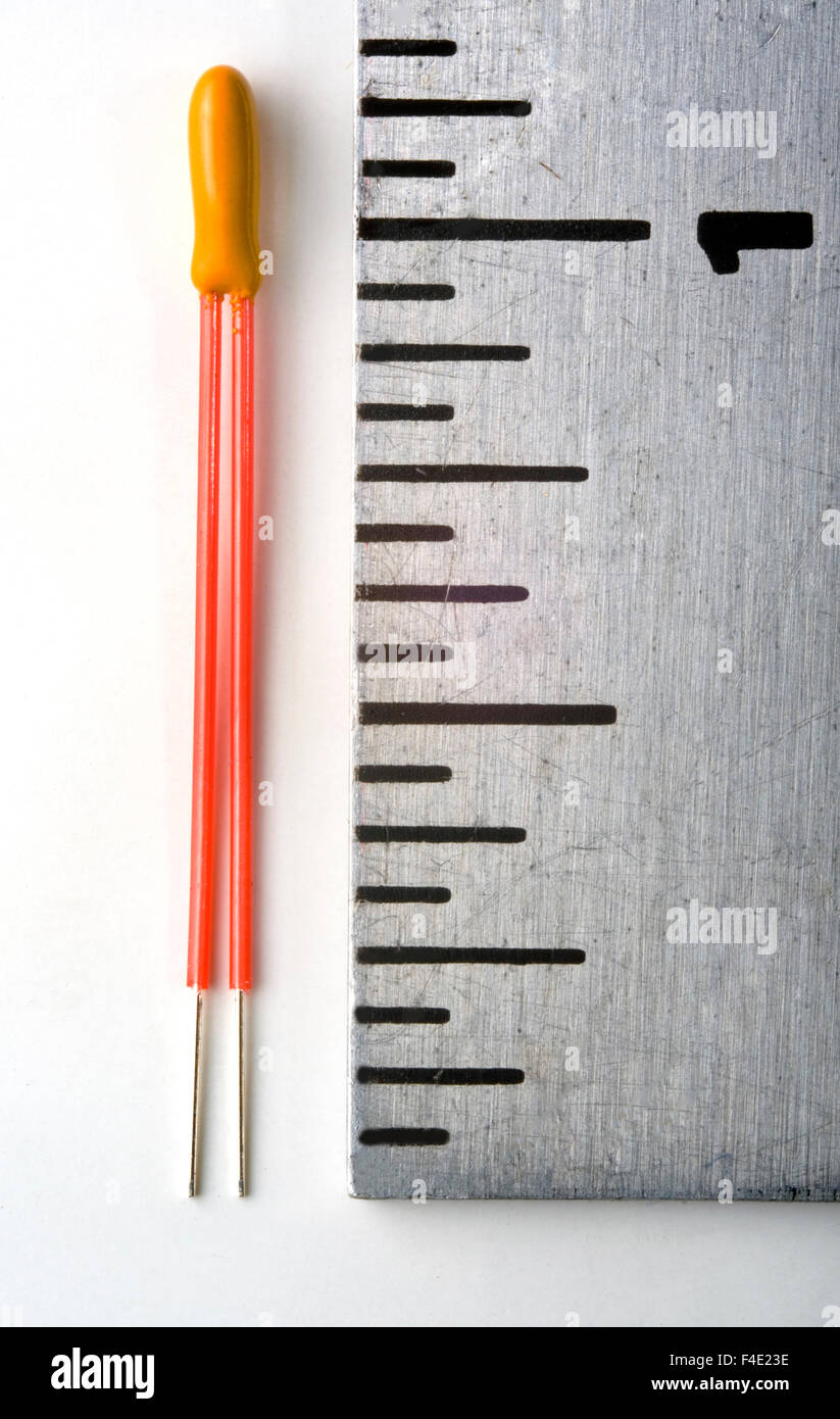 A thermistor is juxtaposed with a ruler to show its small size. It is a type of resistor whose resistance is dependent on temperature. The word is a portmanteau of thermal and resistor Stock Photo