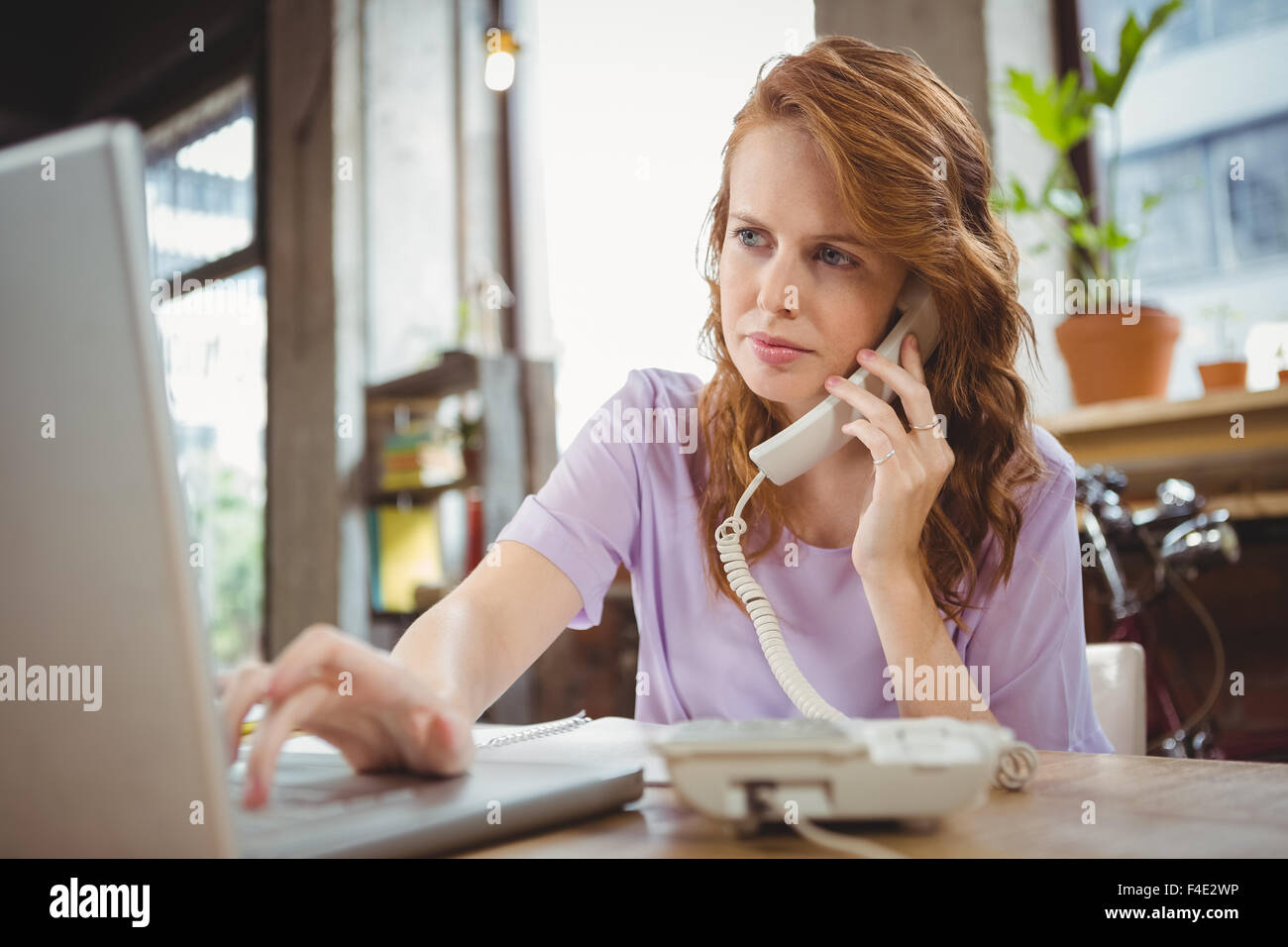 Businesswoman takling on landline while working on laptop Stock Photo