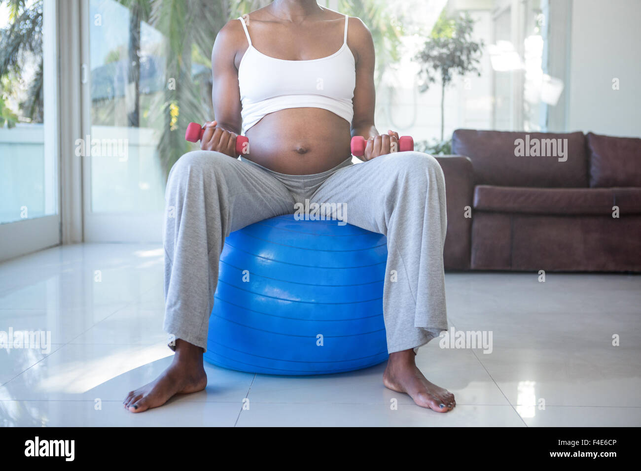 Mid section of pregnant woman with dumbbells sitting on exercise ball Stock Photo
