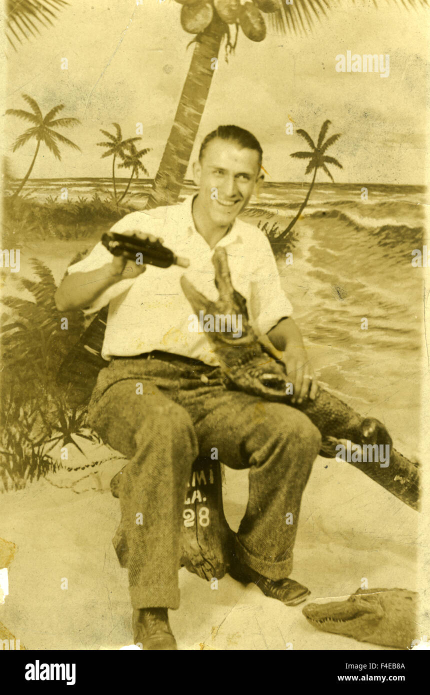 man in his 20s 30s posing with baby alligator in Florida fake palms painting backdrop Stock Photo