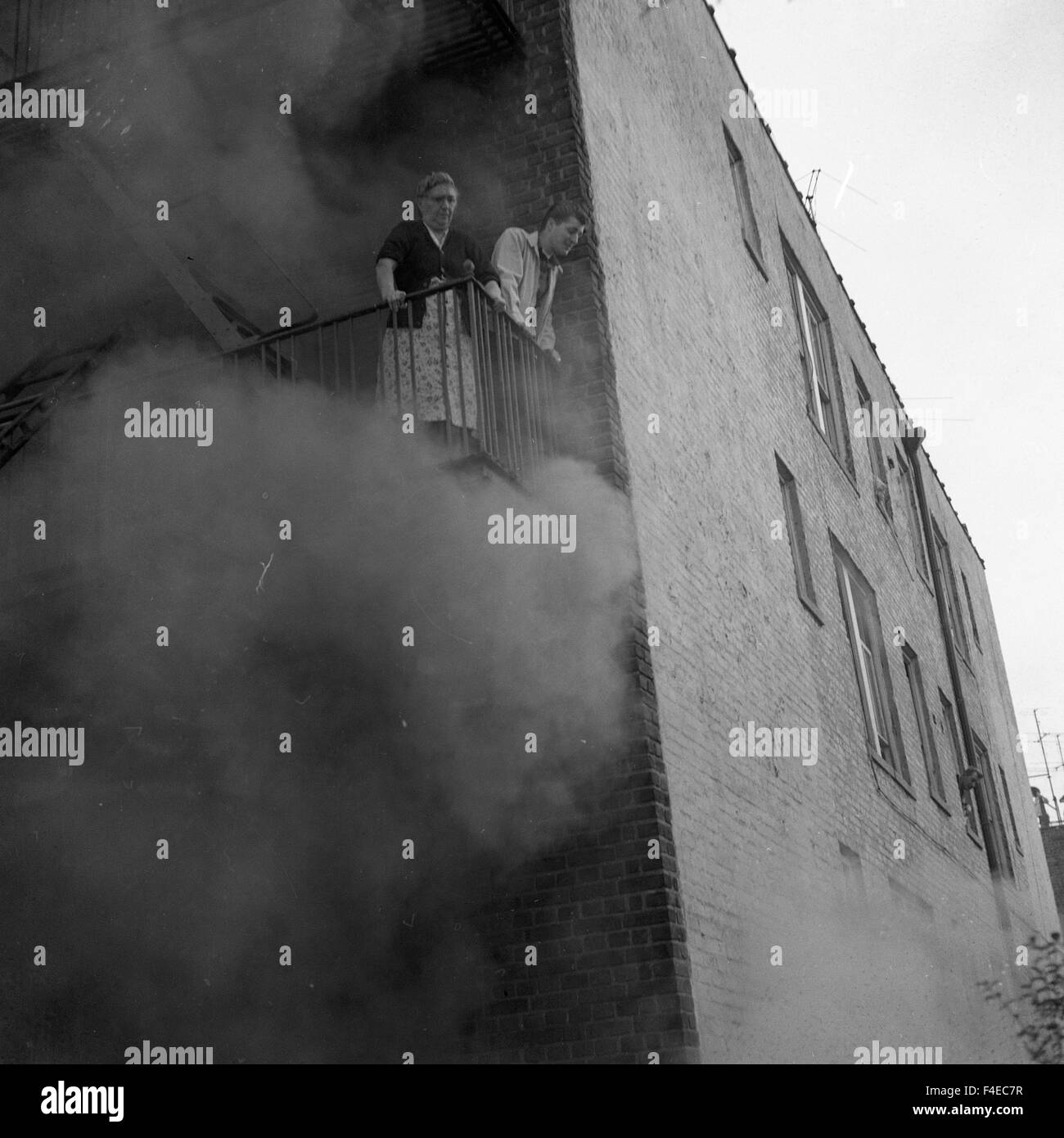 Man and woman trapped on a balcony during an apartment fire looking down for help Stock Photo