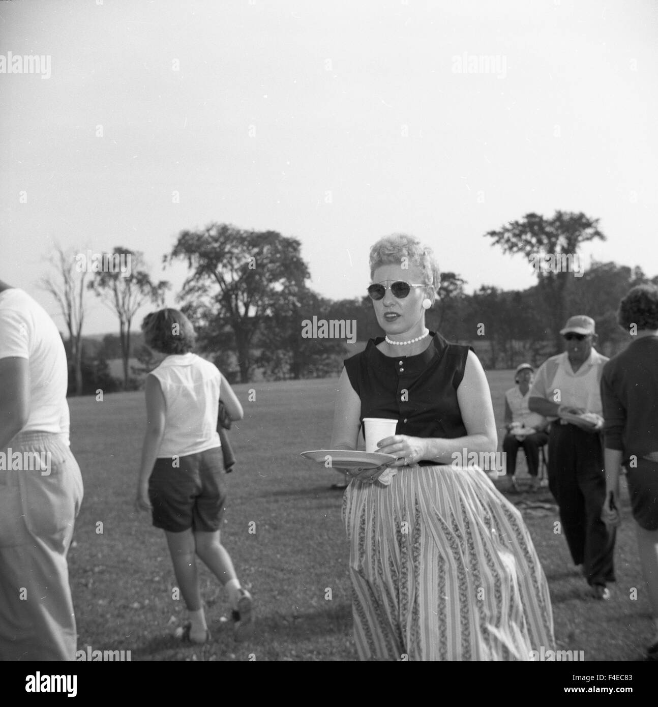 Fashionable woman walking with a plate and cup during a summer picnic Stock Photo