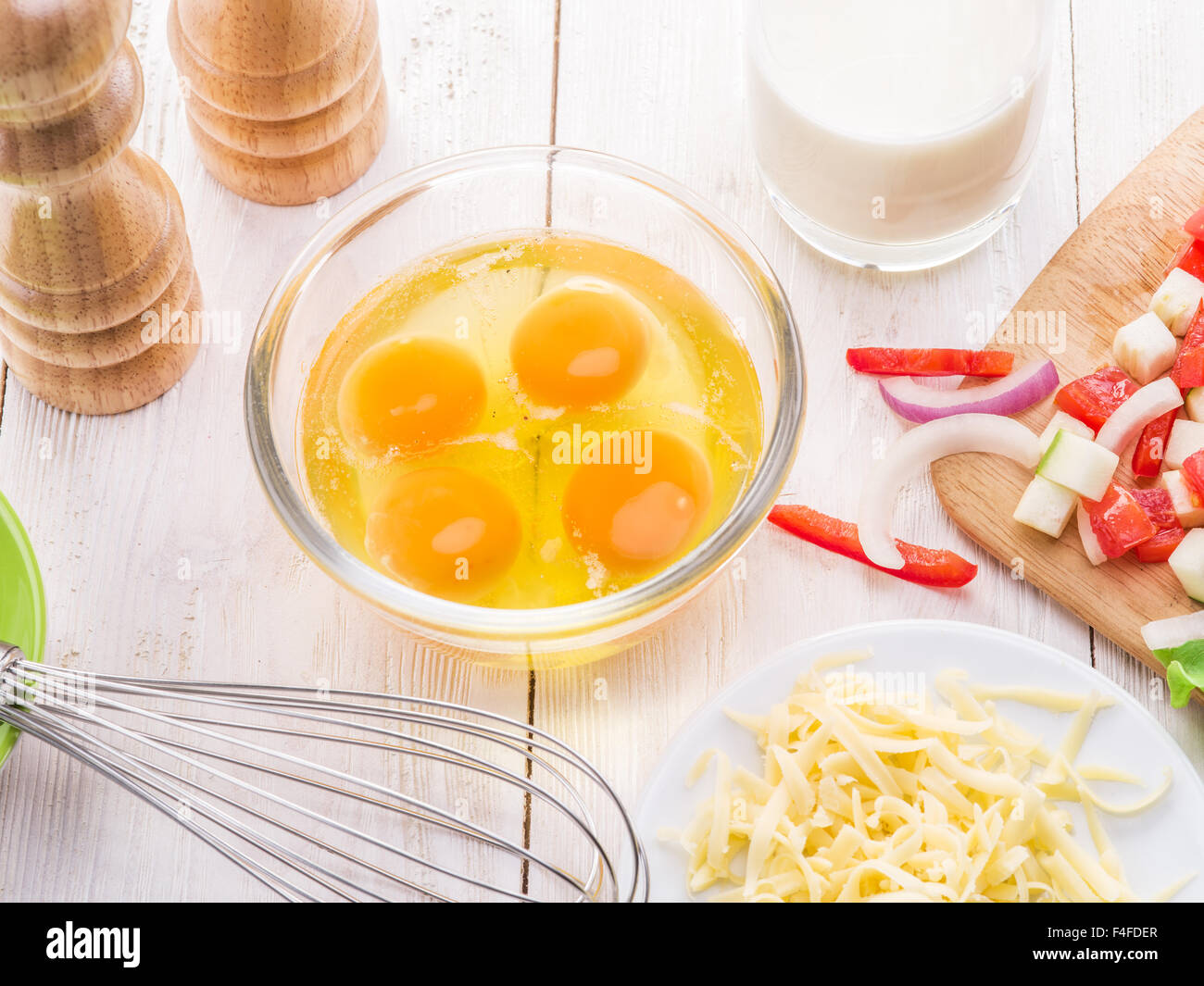 Omelet ingredients: eggs, fresh cut vegetables, milk and cheese on the wooden table. Stock Photo