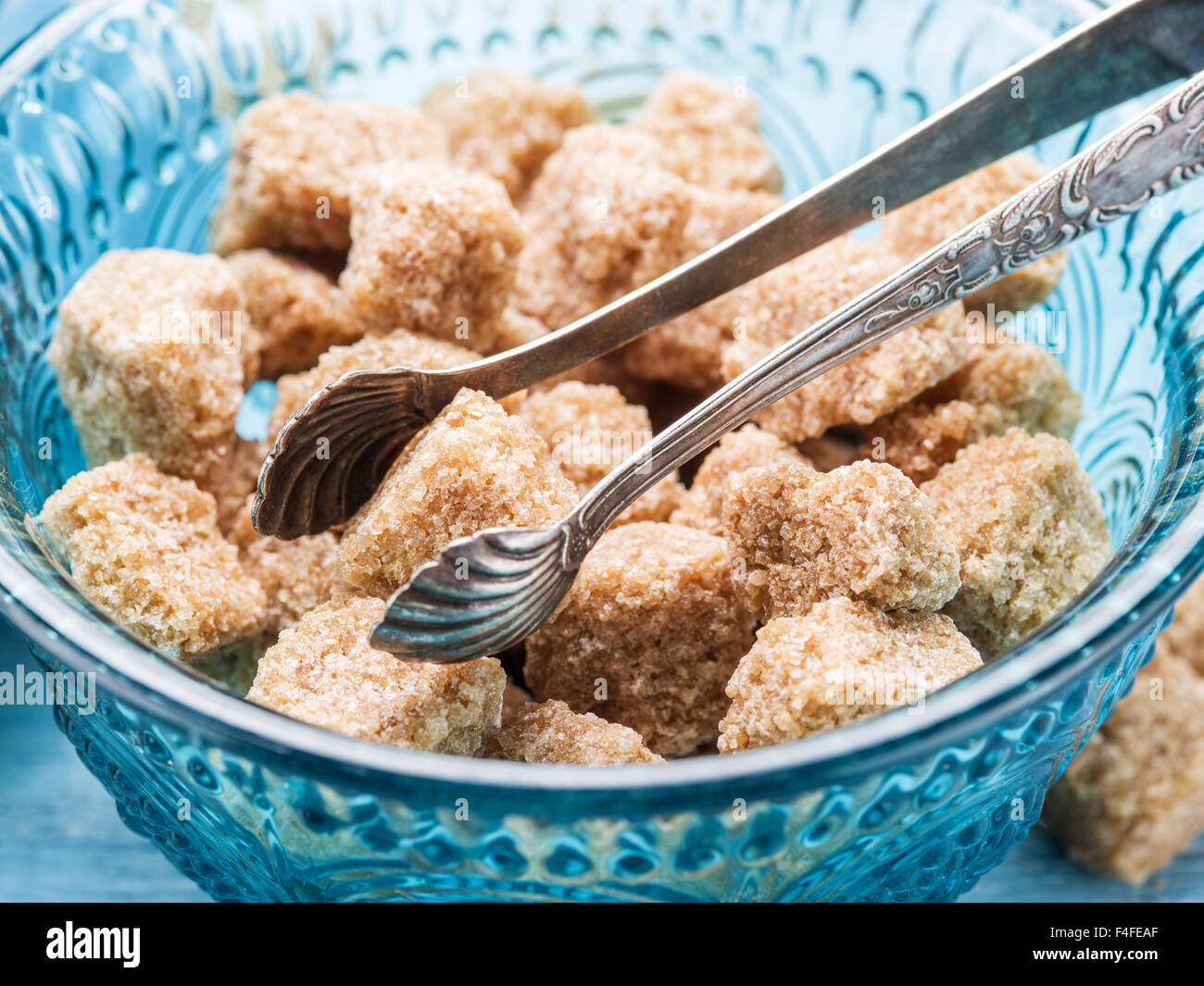 Cane sugar cubes in the old-fashioned glass plate and sugar tongs. Stock Photo