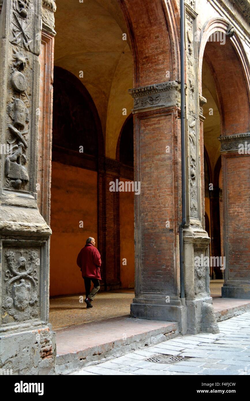 Man in a red coat walking through an arcade in Bologna Italy Stock Photo