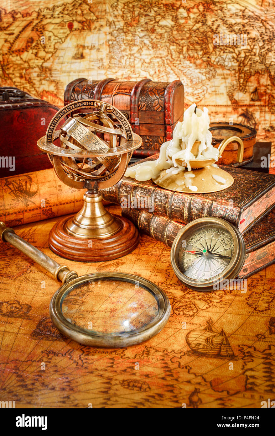 Vintage still life. Vintage magnifying glass lies, pocket watch, old book and armillary sphere on an ancient world map in 1565. Stock Photo