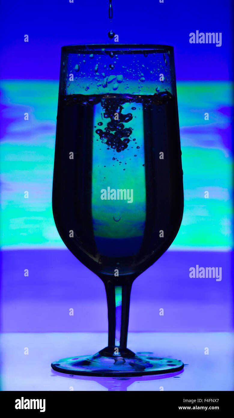 Tinted glass of champagne with splashes of liquid on abstract blurred background in ultraviolet light. Stock Photo