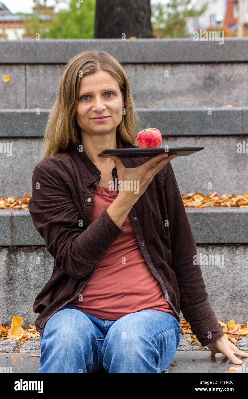 A woman sitting with a tablet -PC and a red apple on a gray stone staircase Stock Photo