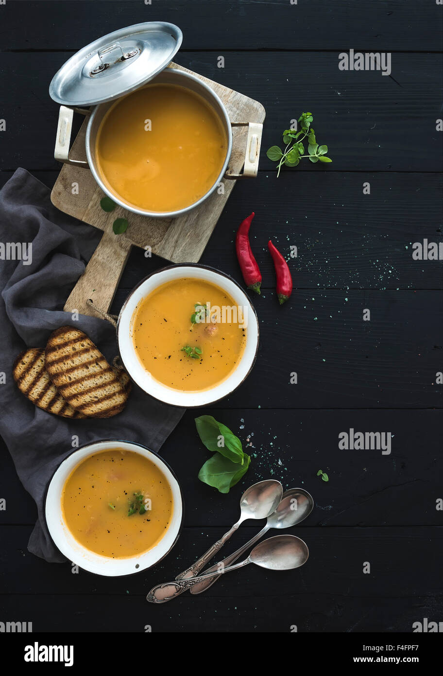 Red lentil soup with spices, herbs, bread in a rustic metal saucepan and bowls, over dark wood backdrop, top view, vertical, cop Stock Photo