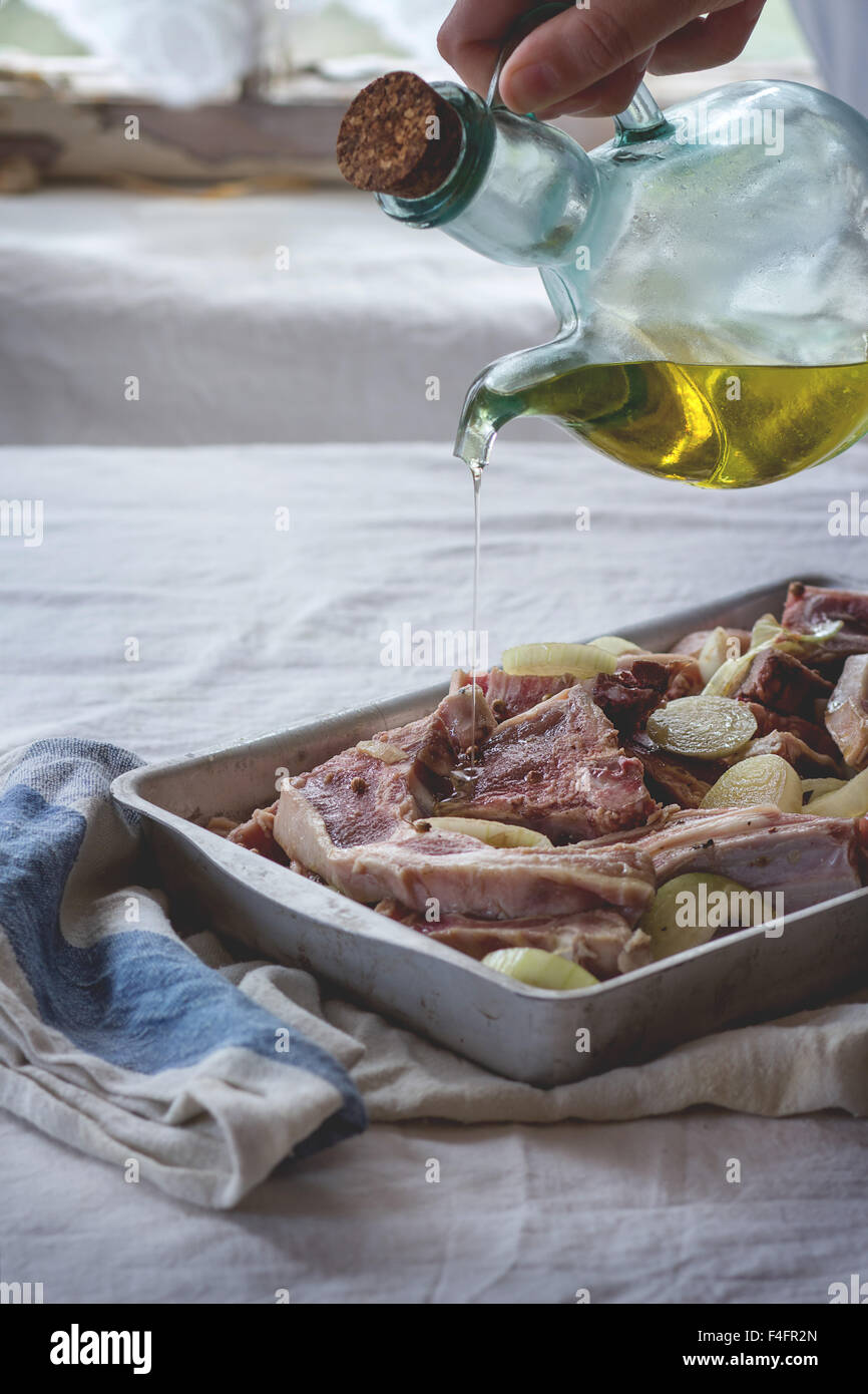 Woman's hand pouring olive oil at marinated raw lamb chops with onion