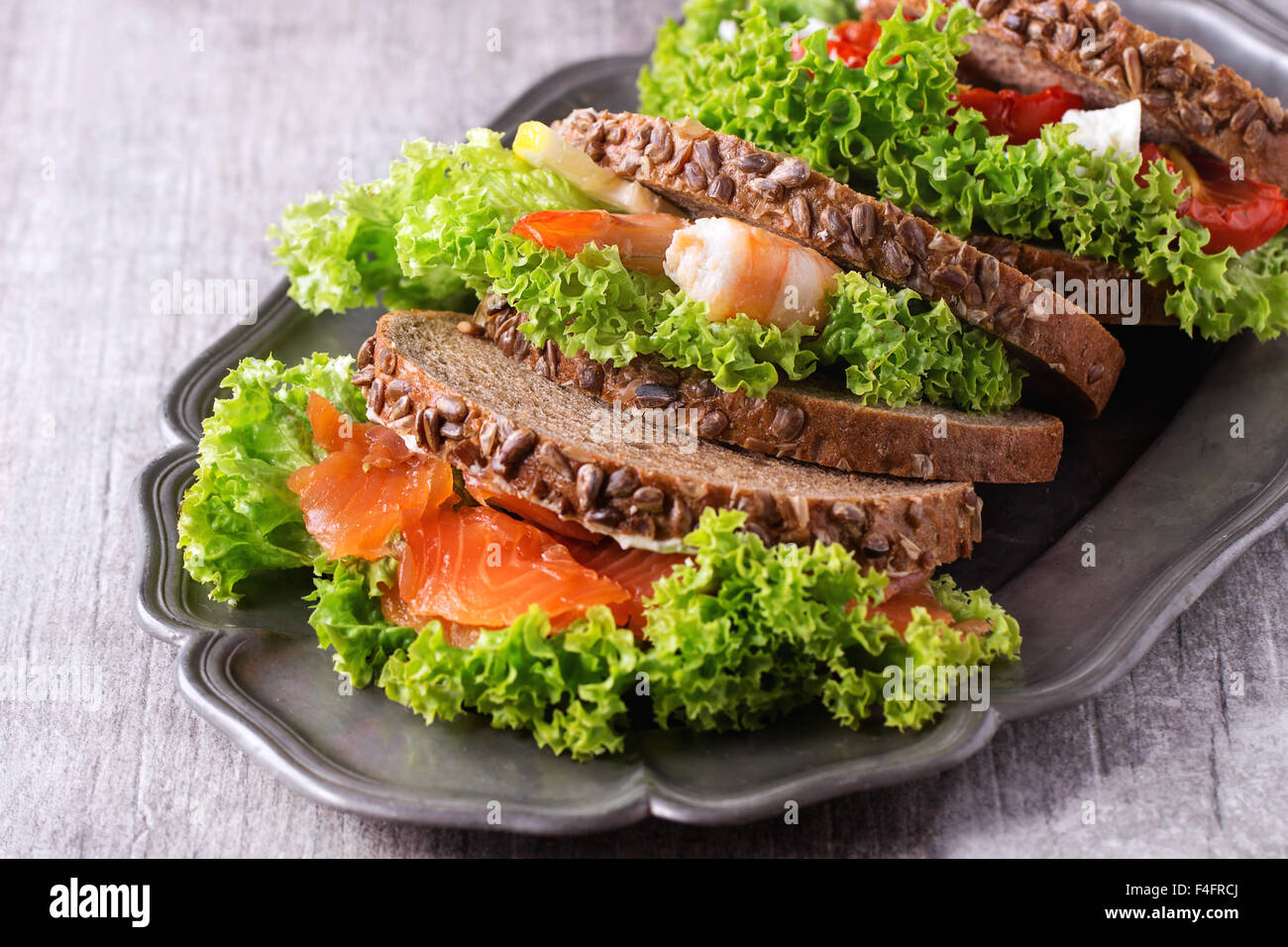 Set of Sandwiches with whole wheat bread, fresh salad, feta cheese, cherry tomatoes, shrimp and salted salmon on vintage metal p Stock Photo