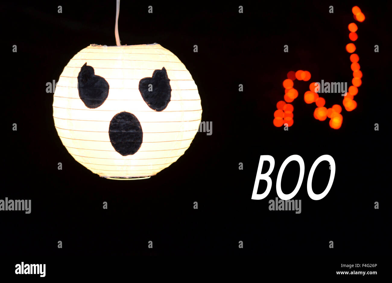 Festive Halloween decorations.  White glowing ghost, pumpkin face with black backdrop.  Orange glowing lights and BOO displayed. Stock Photo
