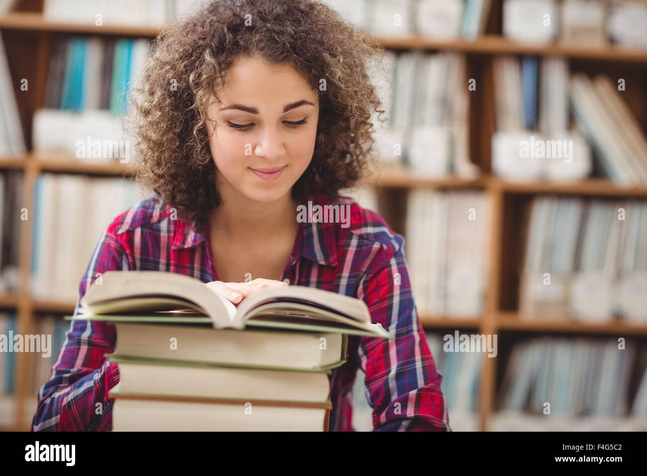 Pretty student in library with pile of books Stock Photo - Alamy
